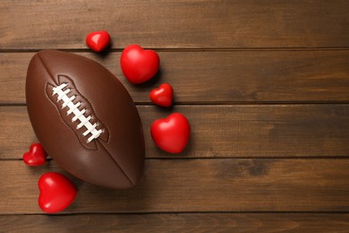 Photo of American football ball and hearts on wooden background, flat lay. Space for text