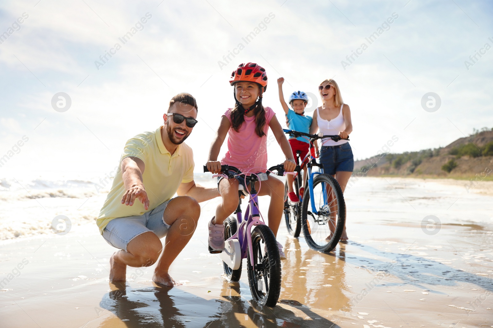 Photo of Happy parents teaching children to ride bicycles on sandy beach near sea