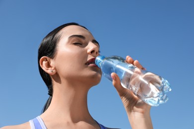 Photo of Beautiful young sportswoman drinking water outdoors, closeup. Refreshing drink