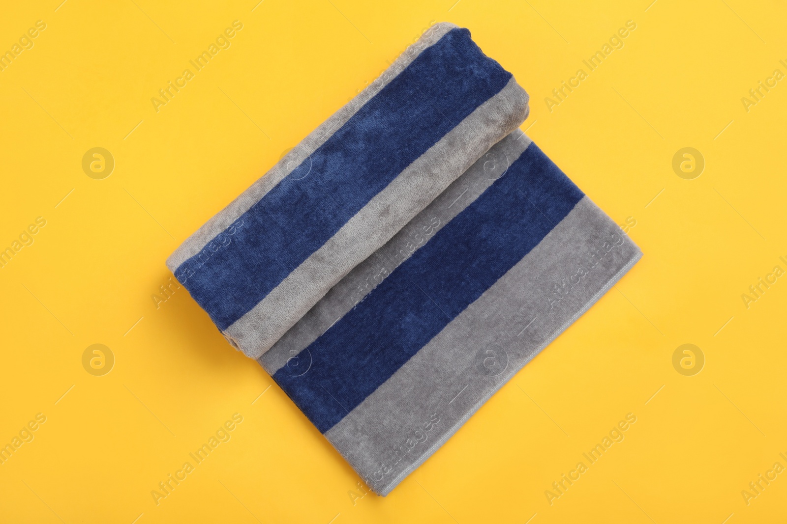 Photo of Rolled striped beach towel on yellow background, top view