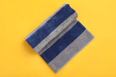 Photo of Rolled striped beach towel on yellow background, top view