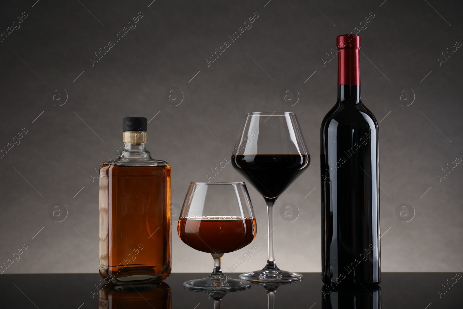 Photo of Bottles and glasses with different alcoholic drinks on table against gray background