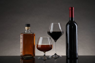 Photo of Bottles and glasses with different alcoholic drinks on table against gray background