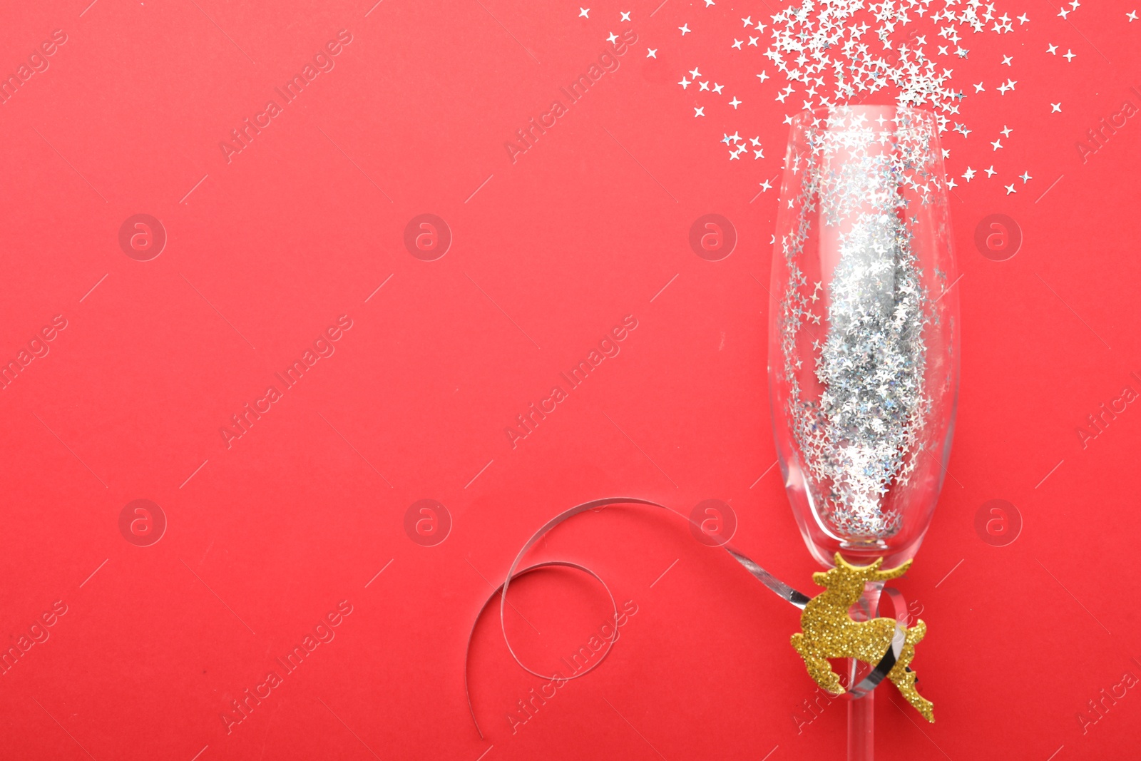Photo of Shiny confetti spilled out of champagne glass on red background, top view. Space for text