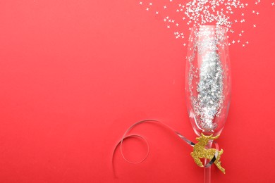 Shiny confetti spilled out of champagne glass on red background, top view. Space for text