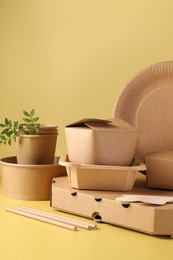 Photo of Eco friendly food packaging. Paper containers, tableware and green twigs on pale yellow background