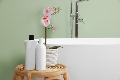 Stylish ceramic tub, care products and beautiful orchid on coffee table in bathroom. Space for text