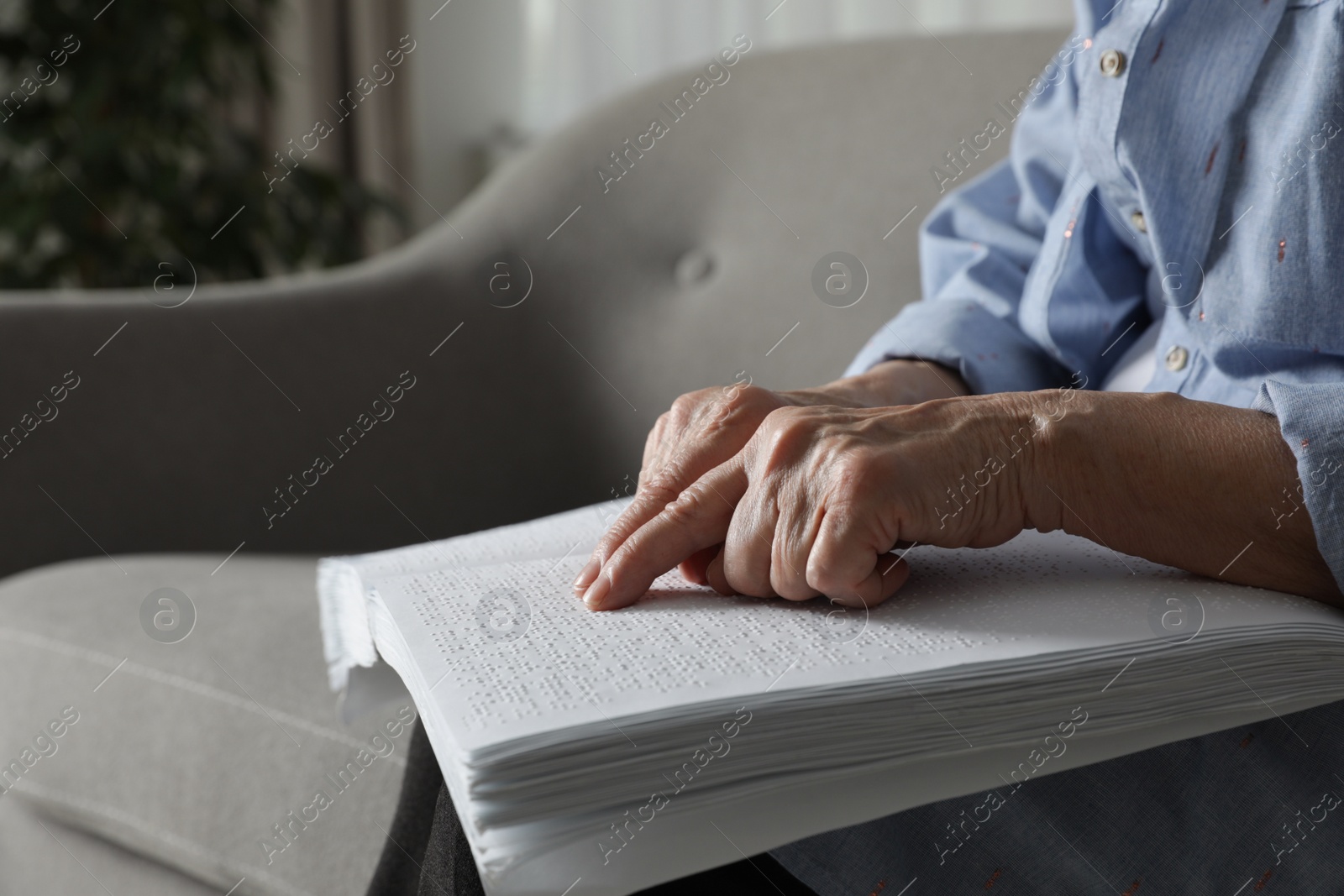 Photo of Blind senior person reading book written in Braille on sofa indoors, closeup. Space for text