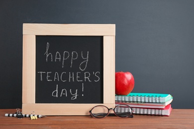 Little blackboard with inscription HAPPY TEACHER'S DAY, notebooks and eyeglasses on table