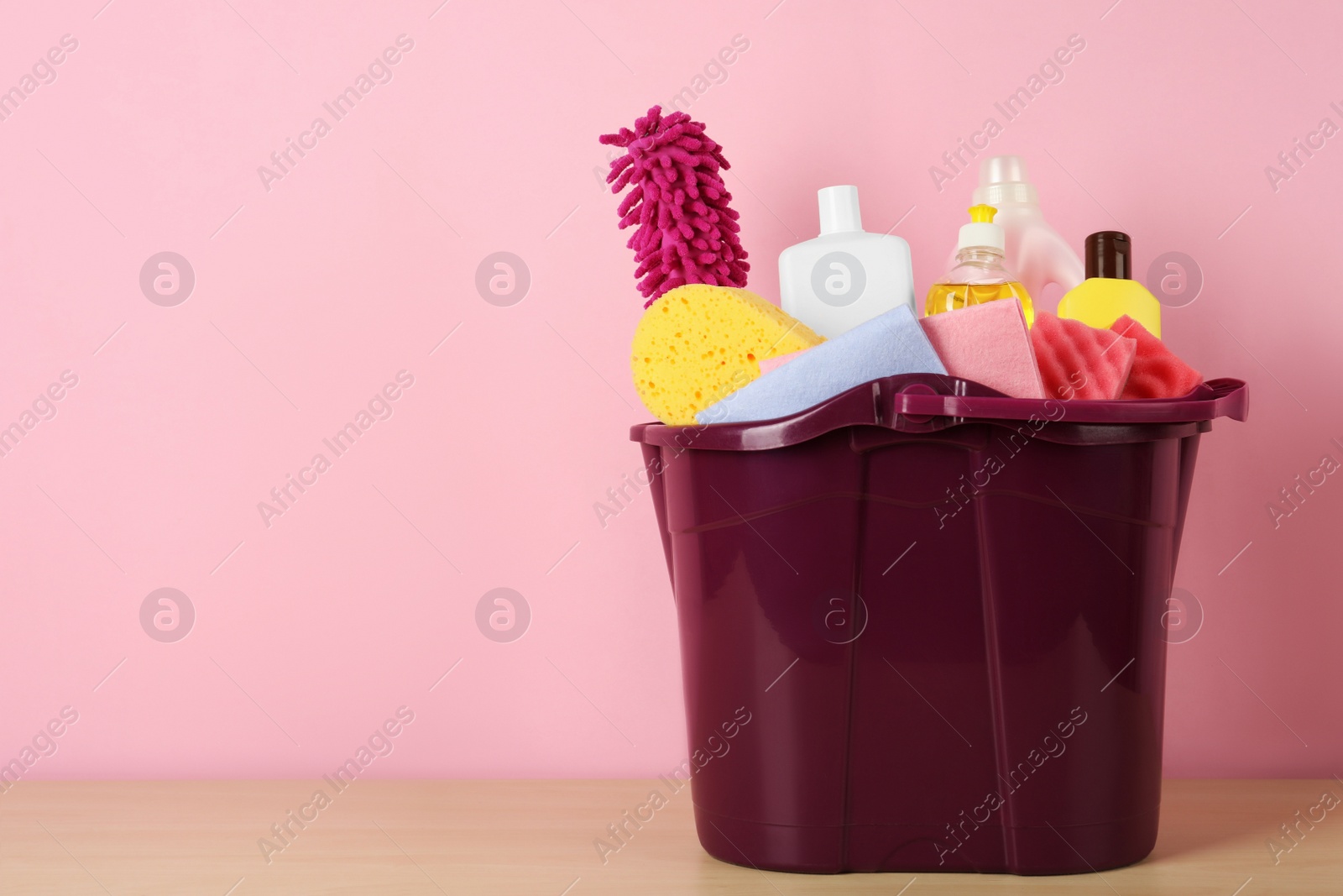 Photo of Bucket with different cleaning supplies on wooden floor near pink wall. Space for text