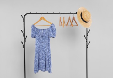 Rack with wicker hat and stylish women`s dress on wooden hanger against light grey background