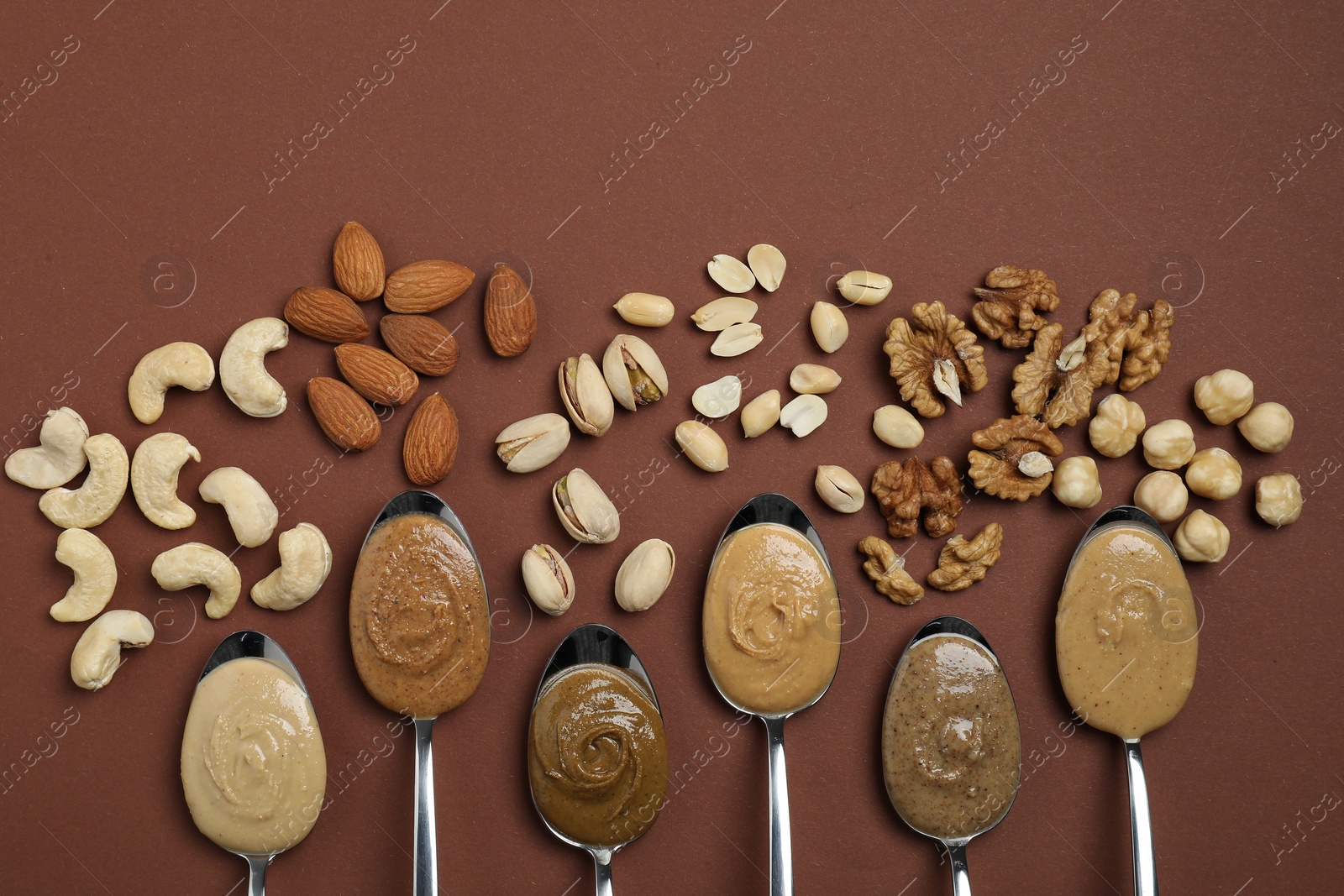 Photo of Tasty nut butters in spoons and raw nuts on brown table, flat lay