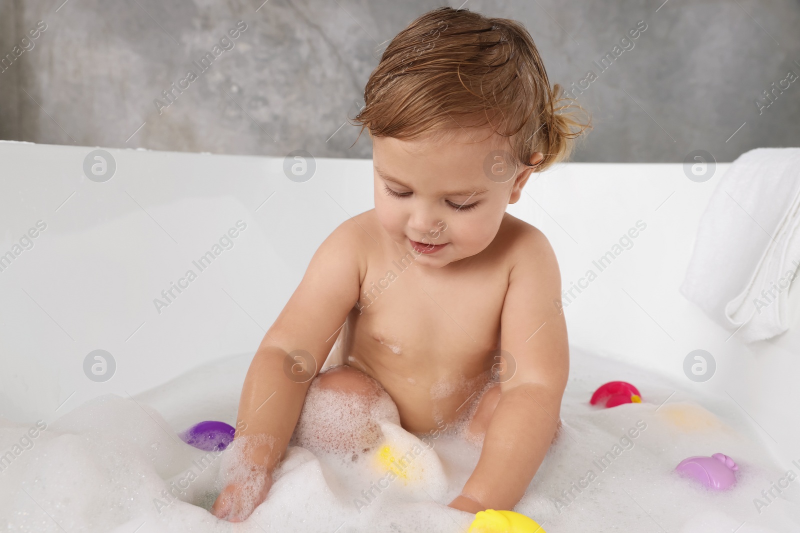 Photo of Cute little girl taking bubble bath with toys indoors