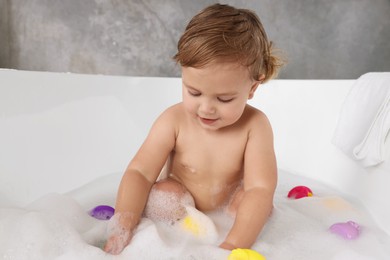 Photo of Cute little girl taking bubble bath with toys indoors