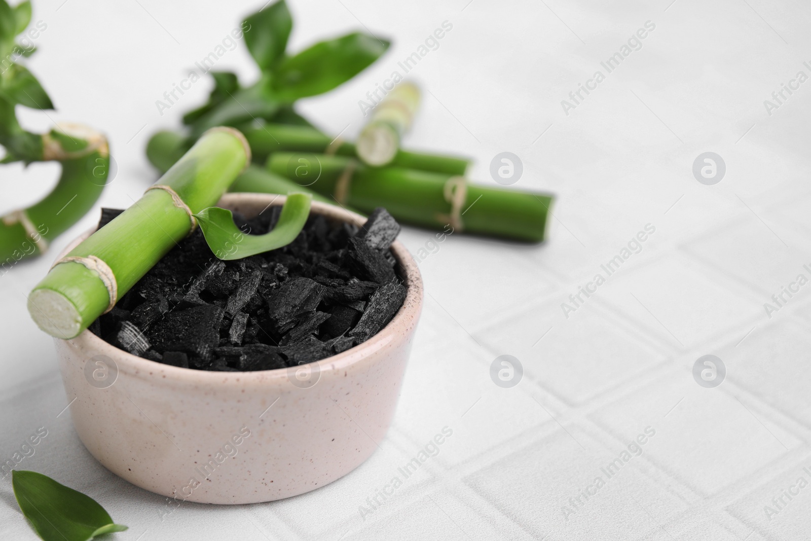 Photo of Fresh bamboo and charcoal on white tiled table, closeup. Space for text