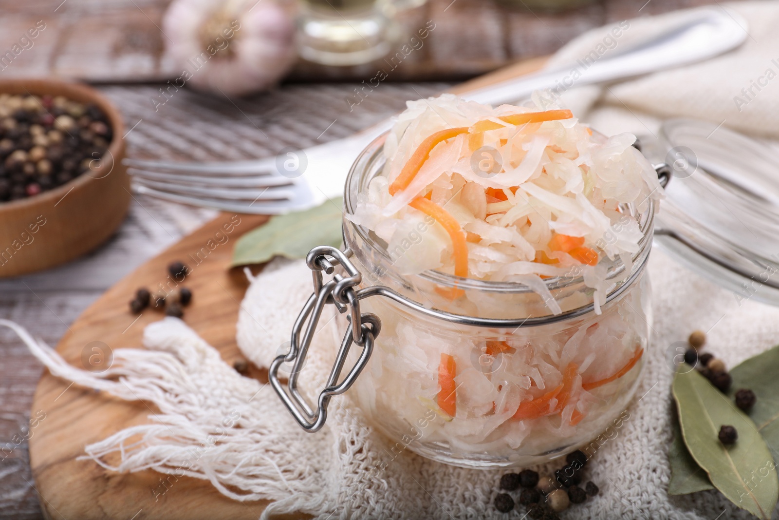 Photo of Glass jar of tasty sauerkraut and ingredients on wooden table