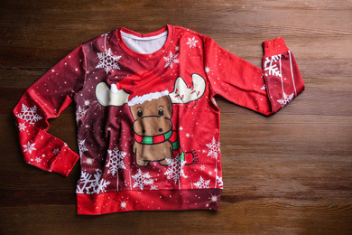 Warm Christmas sweater with deer on wooden table, top view