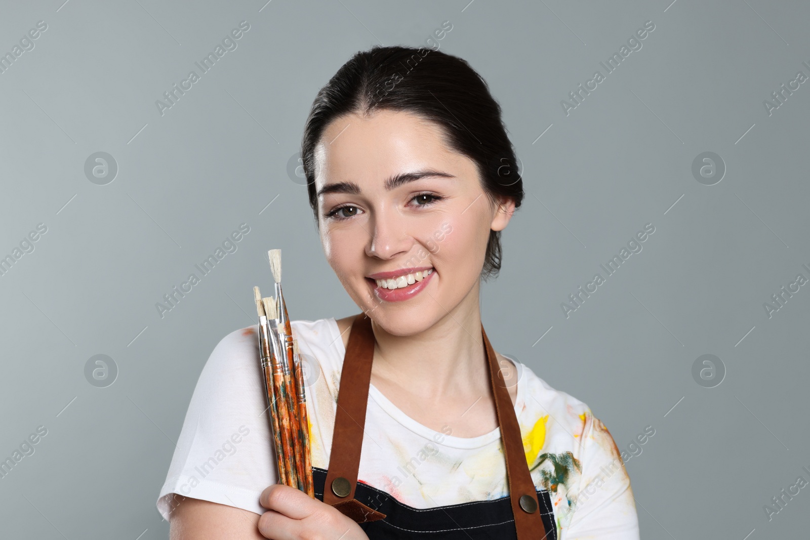 Photo of Woman with paintbrushes on grey background. Young artist