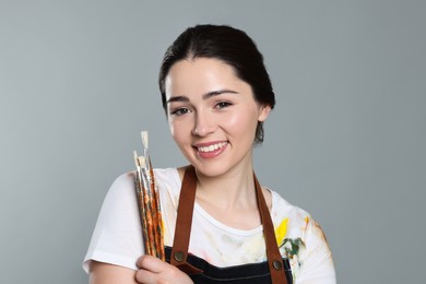 Photo of Woman with paintbrushes on grey background. Young artist