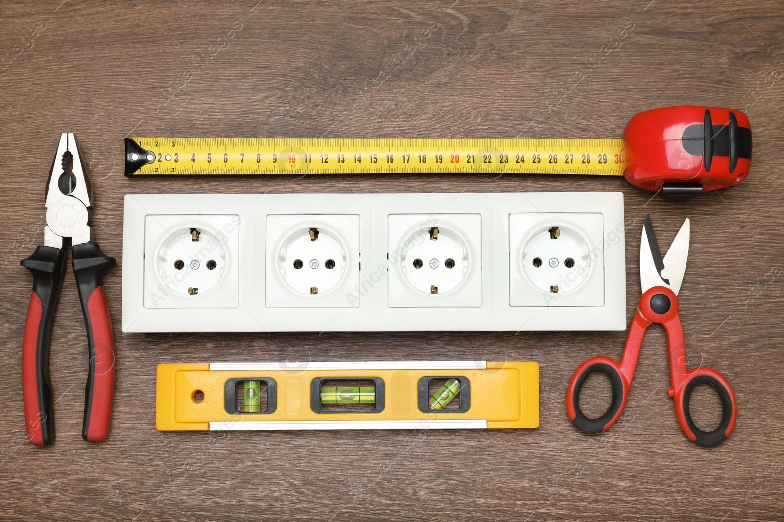 Photo of Power socket and set of electrician's tools on wooden table, flat lay