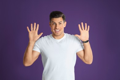 Man showing number ten with his hands on purple background
