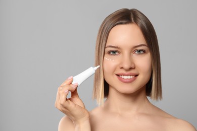 Photo of Young woman applying cream under eyes on light grey background, space for text