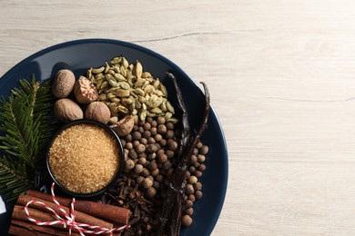 Different aromatic spices and fir branches on light wooden table, top view. Space for text