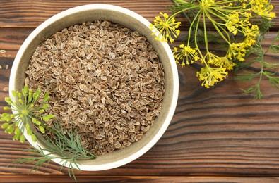 Photo of Bowl of dry seeds and fresh dill on wooden table, flat lay