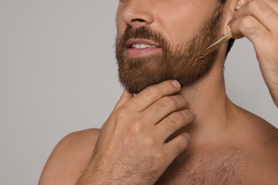 Man applying oil onto beard on grey background, closeup