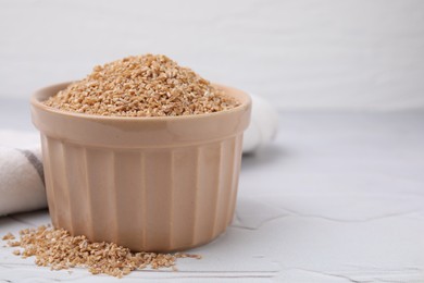 Dry wheat groats in bowl on white textured table, closeup. Space for text