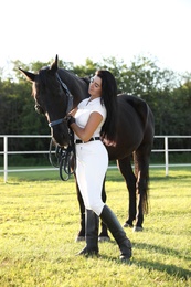 Young woman in horse riding suit and her beautiful pet outdoors on sunny day