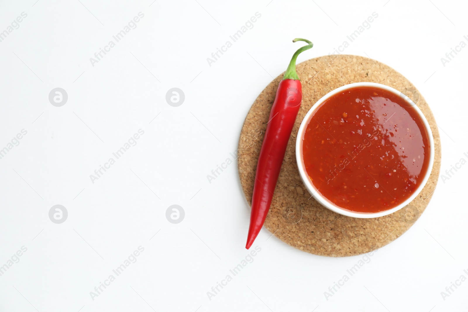 Photo of Spicy chili sauce in bowl and fresh pepper on white background, top view. Space for text