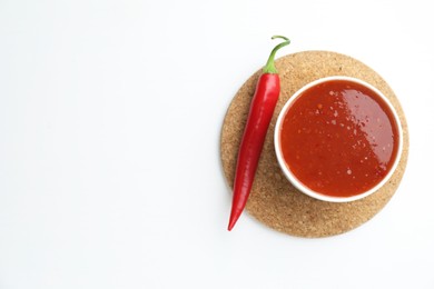 Photo of Spicy chili sauce in bowl and fresh pepper on white background, top view. Space for text