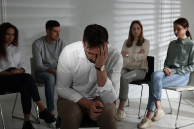 Photo of Unhappy man and group of people behind his back indoors. Therapy session