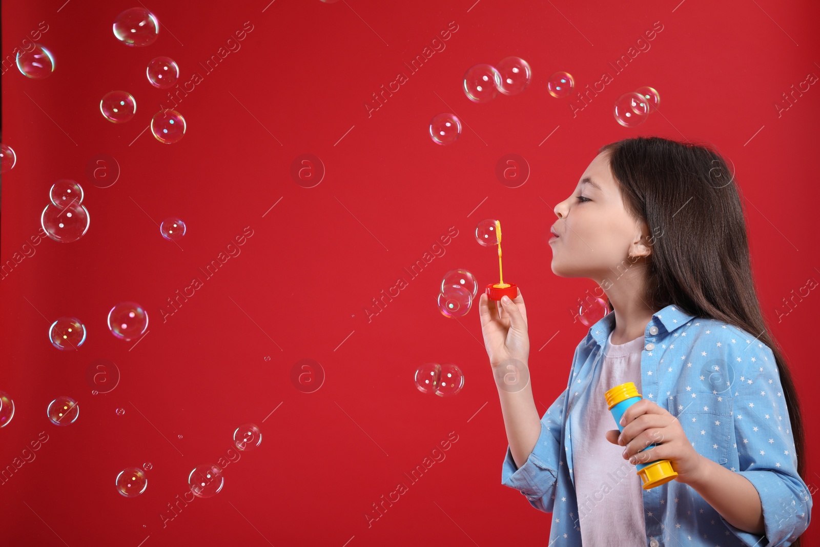 Photo of Little girl blowing soap bubbles on red background