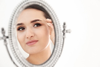 Photo of Young woman plucking eyebrow with tweezers in front of mirror