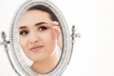 Young woman plucking eyebrow with tweezers in front of mirror