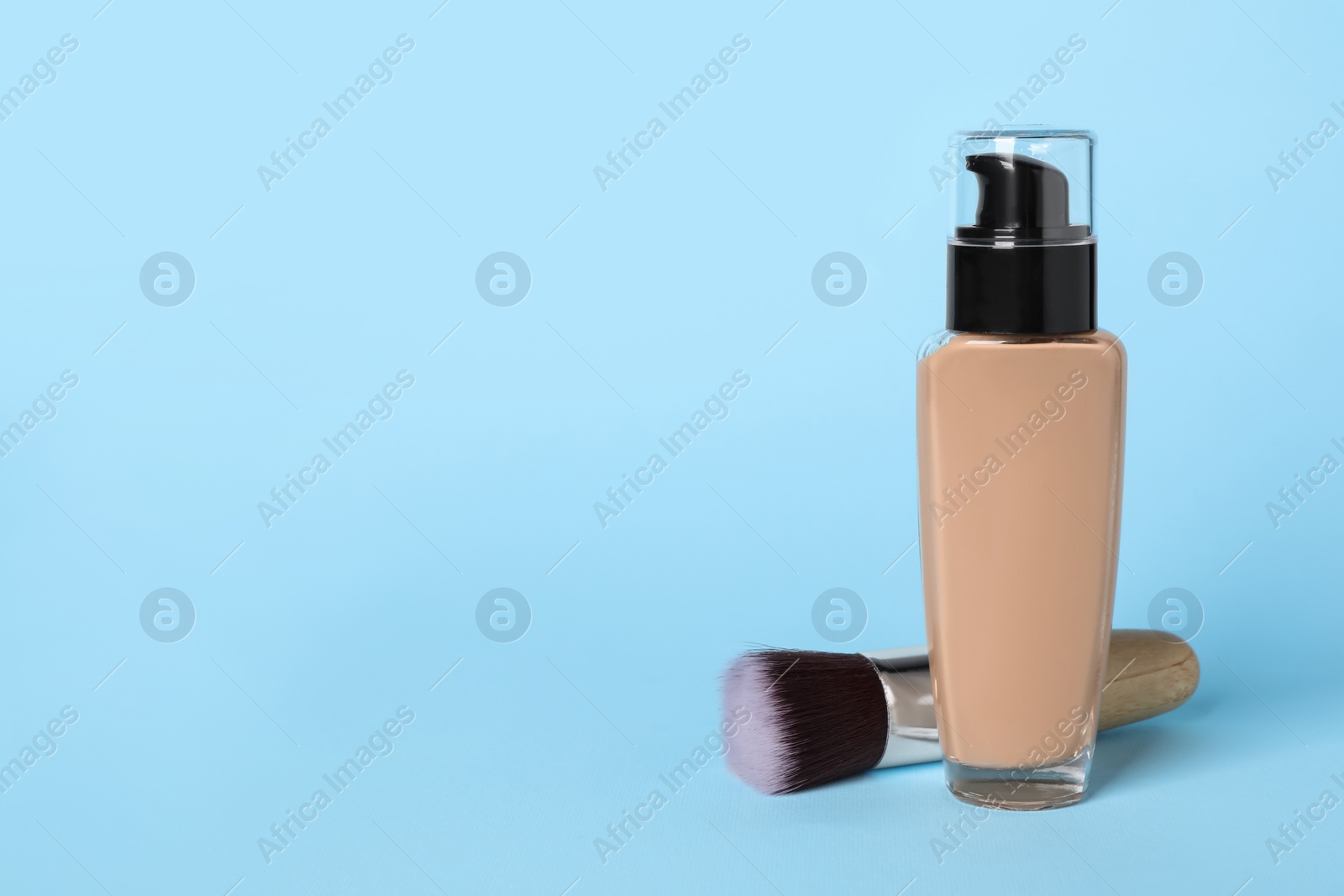Photo of Bottle of skin foundation and brush on light blue background, space for text. Makeup product