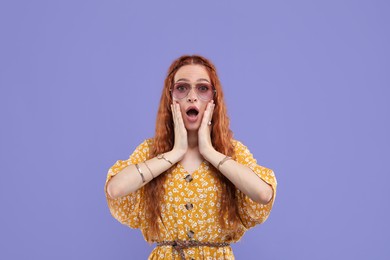 Photo of Surprised young hippie woman in sunglasses on violet background