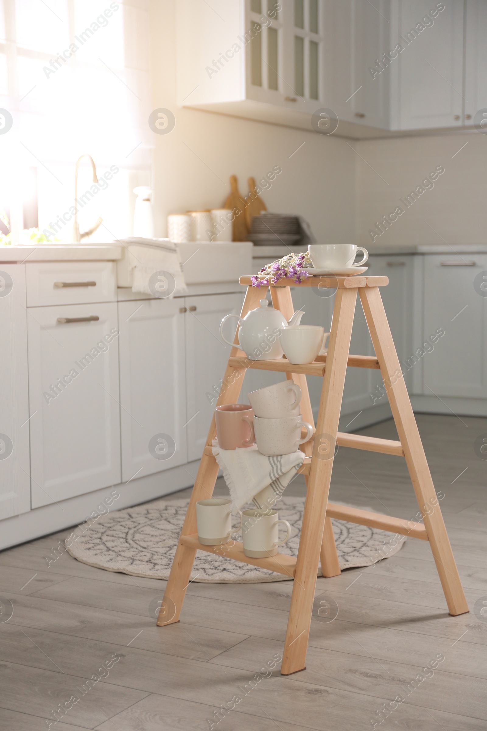 Photo of Decorative ladder with different dishware and field flowers bouquet in stylish kitchen. Idea for interior design