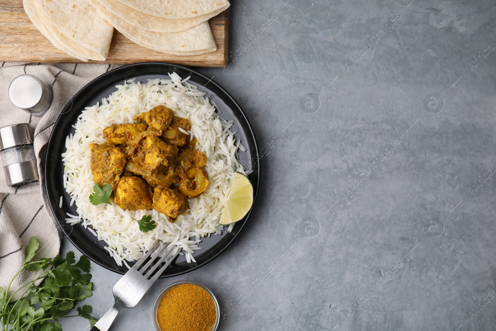 Photo of Delicious chicken curry with rice and ingredients on grey table, flat lay. Space for text