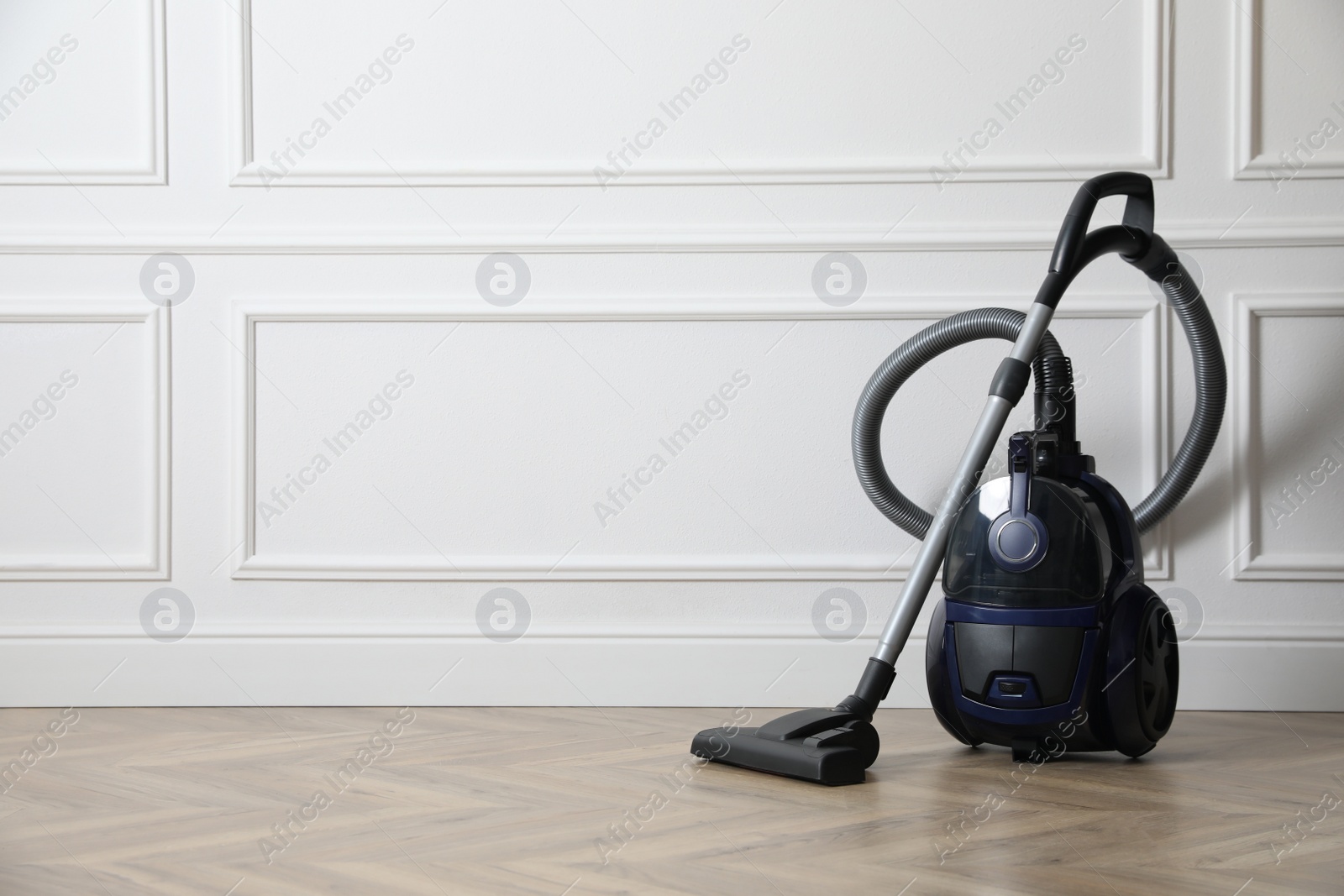 Photo of Modern vacuum cleaner near white wall indoors, space for text