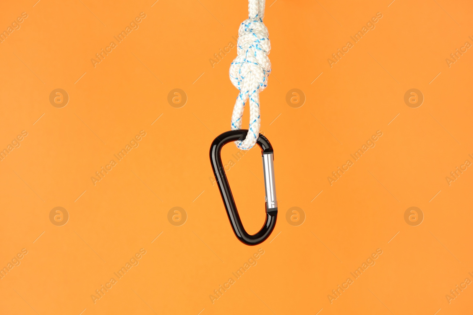 Photo of One metal carabiner hanging on rope against orange background