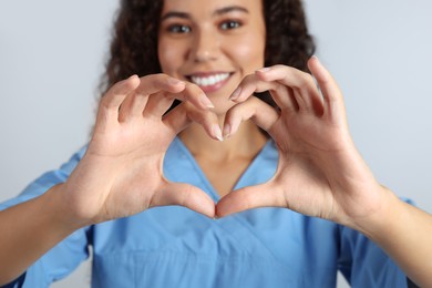 Photo of Happy young African-American doctor making heart with hands on light grey background, closeup