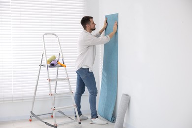 Man hanging light blue wallpaper in room