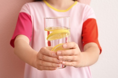 Photo of Young woman holding glass of lemon water on color background, closeup