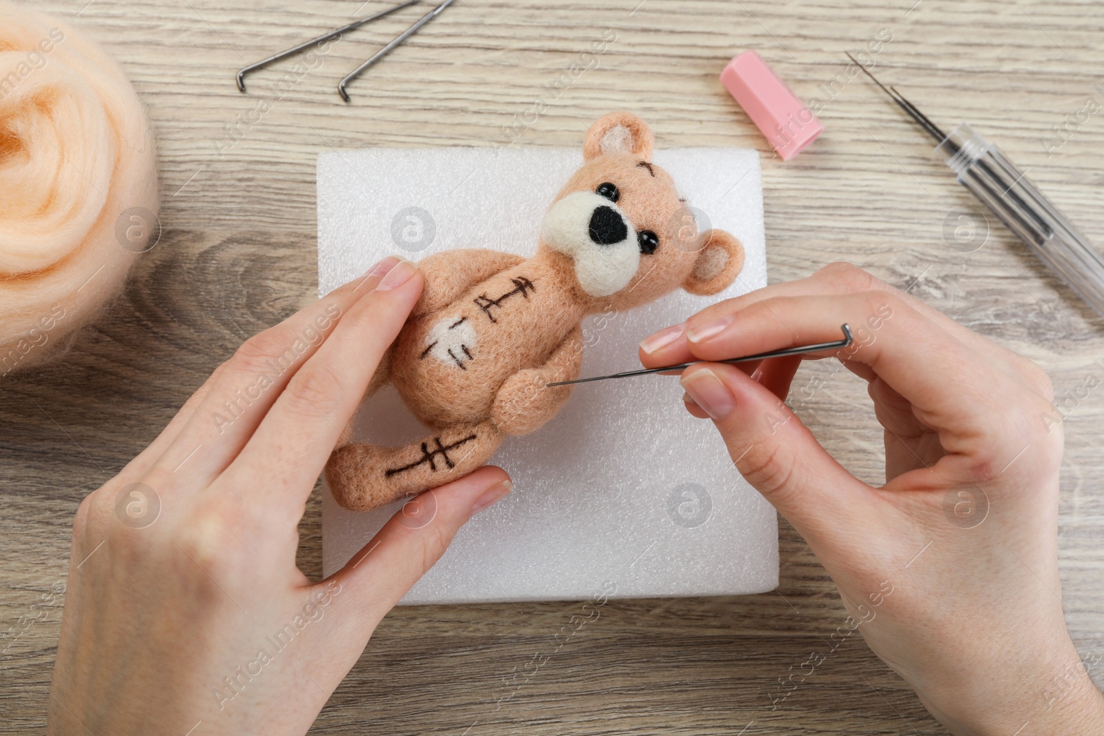 Photo of Woman felting cute toy bear from wool at wooden table, top view