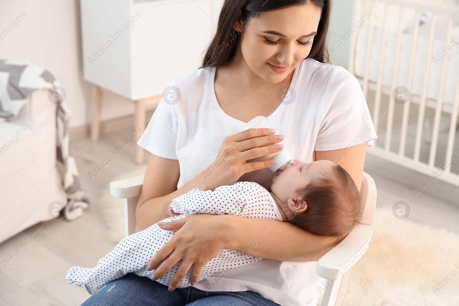 Photo of Woman feeding her baby from bottle in nursery at home