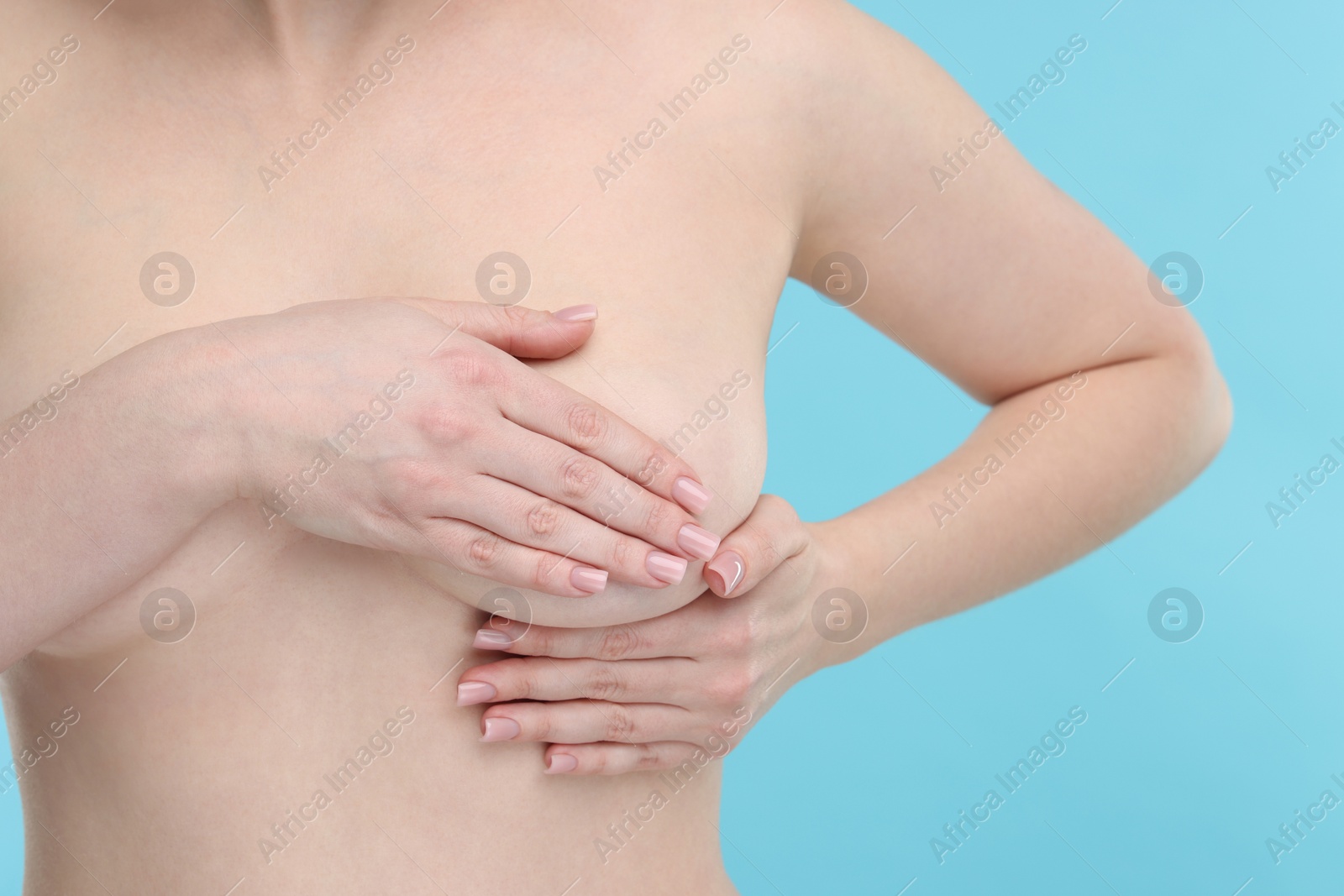 Photo of Mammology. Naked young woman doing breast self-examination on light blue background, closeup