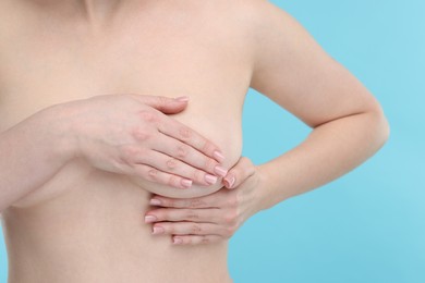 Photo of Mammology. Naked young woman doing breast self-examination on light blue background, closeup